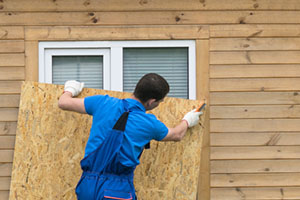 a man obstructs a window with a large piece of plywood