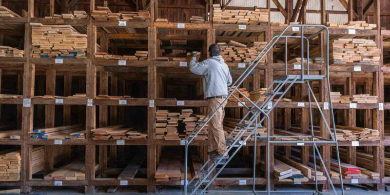 man choosing wood among stacks of lumber on a rack for sale to consumers at a retail hardwood lumber business